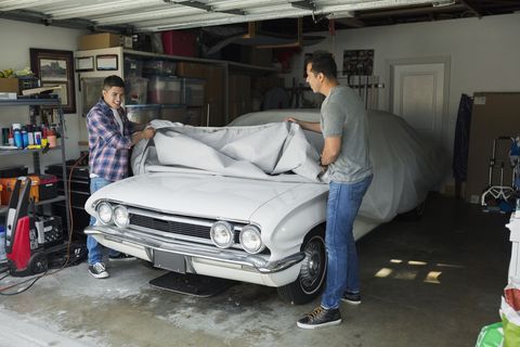 Father and son uncovering vintage car in garage