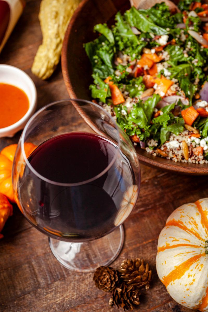 Warm Sweet Potato Salad Bowl, Trader Joe's Platinum Reserve Pinot Noir Carneros 2018 |Trader Joe's Warm Sweet Potato Salad Bowl Recipe | Trader Joe's Wine by popular D.C. lifestyle blogger, Alicia Tenise: image of a wine glass half filled with Trader Joe's Pinot Noir wine lass, mini pumpkins and a wooden bowl filled with warm sweet potato salad.