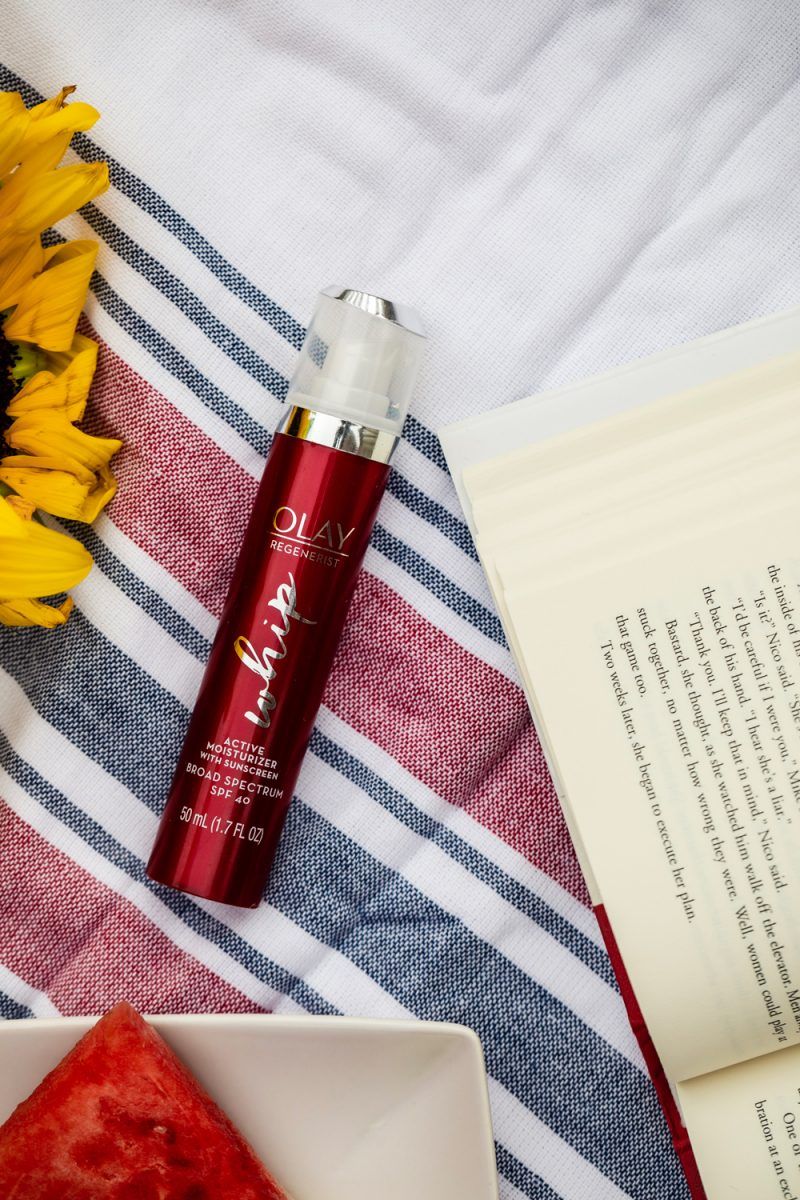 Olay Regenerist Whip review and summer self care routine featured by top D.C beauty blogger, Alicia Tenise | Self Care Routine by popular D.C. lifestyle blog, Alicia Tenise: image of a bottle of Olay Regenerist whip on a red, white, and blue stripe turkish towel next to a open book and a white plate with a watermelon slice on it.
