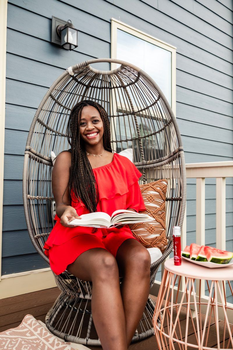 Olay Regenerist Whip review and summer self care routine featured by top D.C beauty blogger, Alicia Tenise | Self Care Routine by popular D.C. lifestyle blog, Alicia Tenise: image of Alicia Tenise wearing a red ruffle dress and sitting in a rattan chair next to a end table that has a plate of sliced watermelon and a bottle of Olay Rengenerist Whip on it.