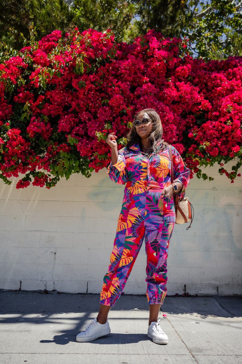 Farm Rio Macaw Twill Jumpsuits, Krewe SONIAT Sunglasses | Summer Jumpsuit by popular LA fashion blogger, Alicia Tenise: image of a woman wearing a summer jumpsuit with a pair of white sneakers and standing under a pink floral plant.
