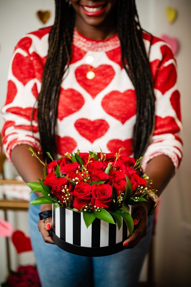 How to Style a Galentine's Day Bar Cart by popular DC lifestyle blogger, Alicia Tenise: image of a woman wearing a Lou & Grey Heart You Sweater and holding red roses in a black and white striped hat box.