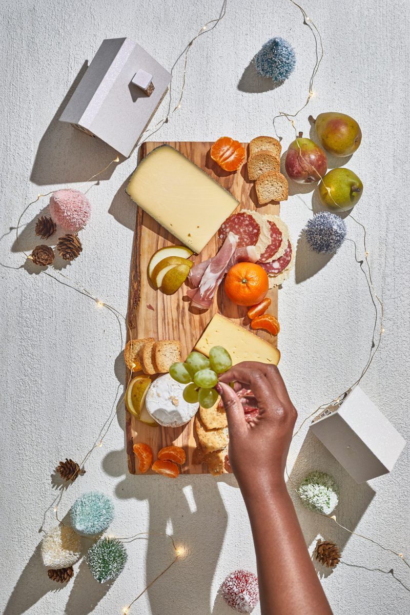 Charcuterie Board by popular D.C. lifestyle blogger, Alicia Tenise: image of Alicia Tenise placing cheese wedges, fruit, and specialty meats down on a wooden board.