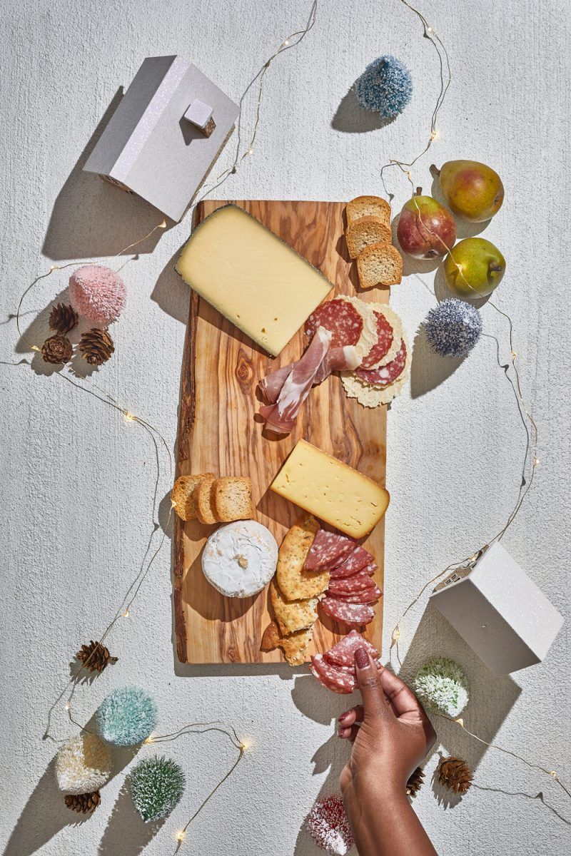 Charcuterie Board by popular D.C. lifestyle blogger, Alicia Tenise: image of Alicia Tenise placing cheese wedges and specialty meats down on a wooden board.