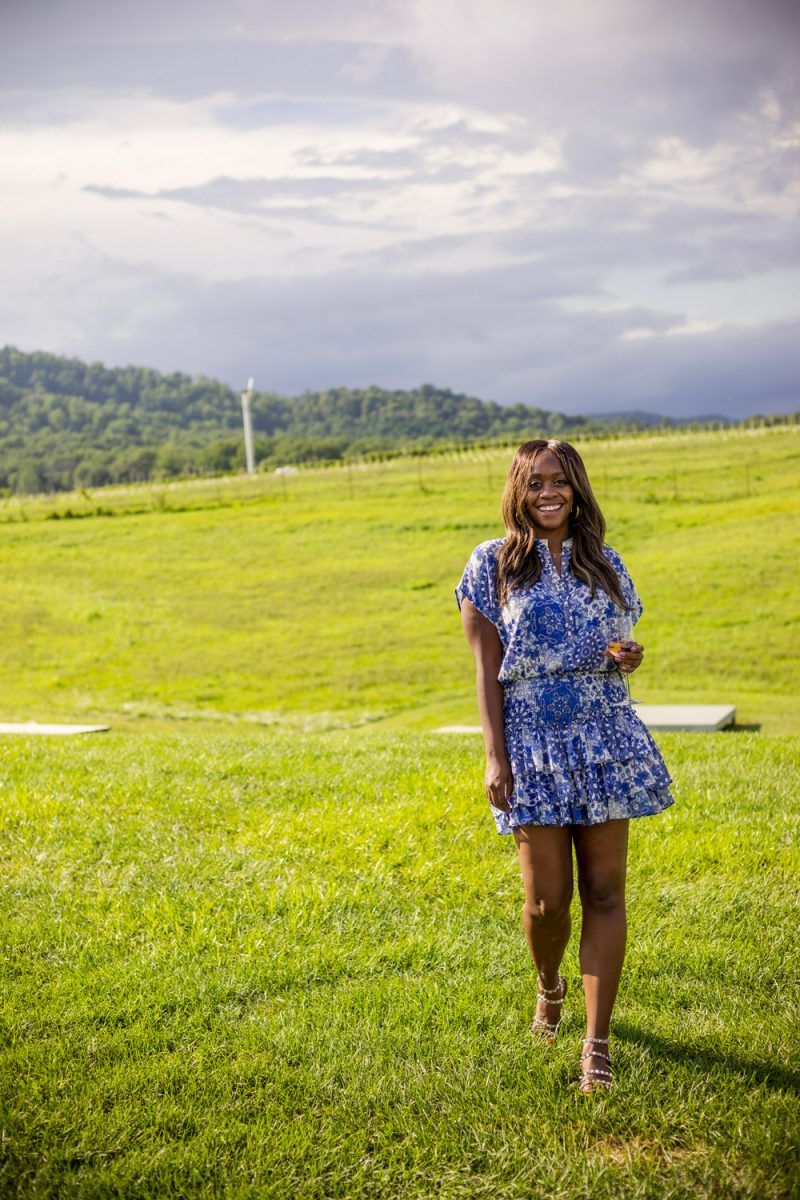Early Mountain Vineyards | Wine 101 by popular D.C. lifestyle blogger, Alicia Tenise: image of Alicia Tenise standing outside at a winery and wearing a Eloisa Dress MISA Los Angeles brand: MISA Los Angeles, Steve Madden Women's Travel Rock Stud Flat Sandals, GOLD DORADO MIYUKI BEADS APPLE WATCH STRAP, and The Sis Kiss It’s All in a Name™ Personalized Necklace while holding a glass of wine.
