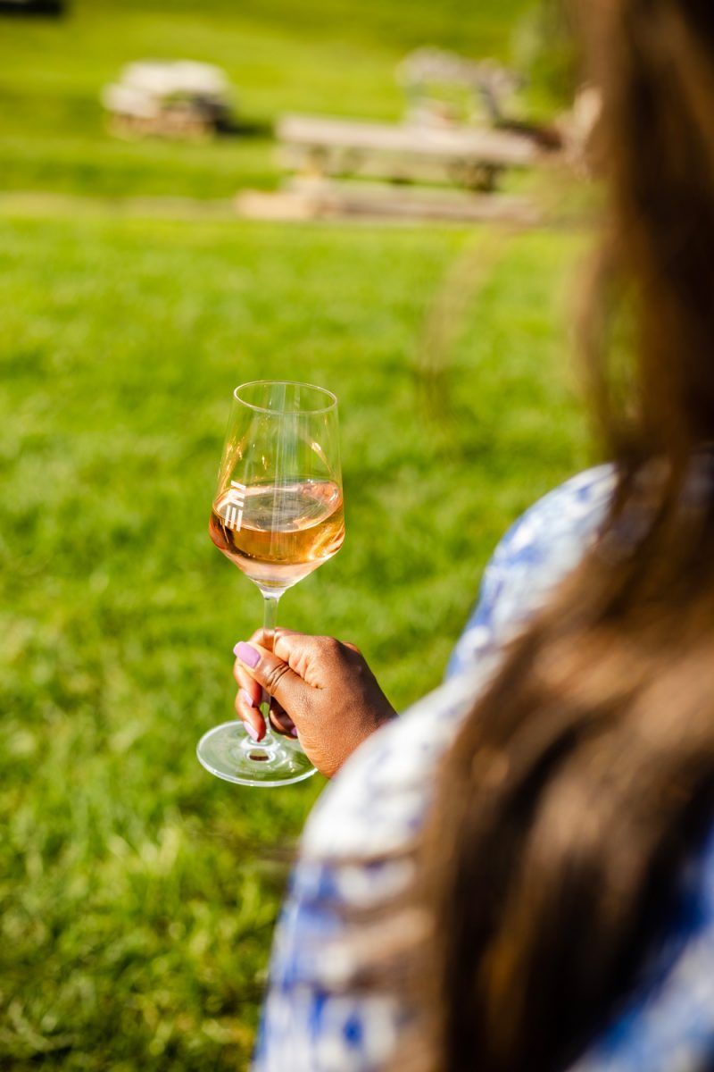 Wine Tasting 101, Early Mountain Vineyards | Wine 101 by popular D.C. lifestyle blogger, Alicia Tenise: image of Alicia Tenise standing outside at a winery and wearing a Eloisa Dress MISA Los Angeles brand: MISA Los Angeles, Steve Madden Women's Travel Rock Stud Flat Sandals, GOLD DORADO MIYUKI BEADS APPLE WATCH STRAP, and The Sis Kiss It’s All in a Name™ Personalized Necklace while holding a glass of wine.