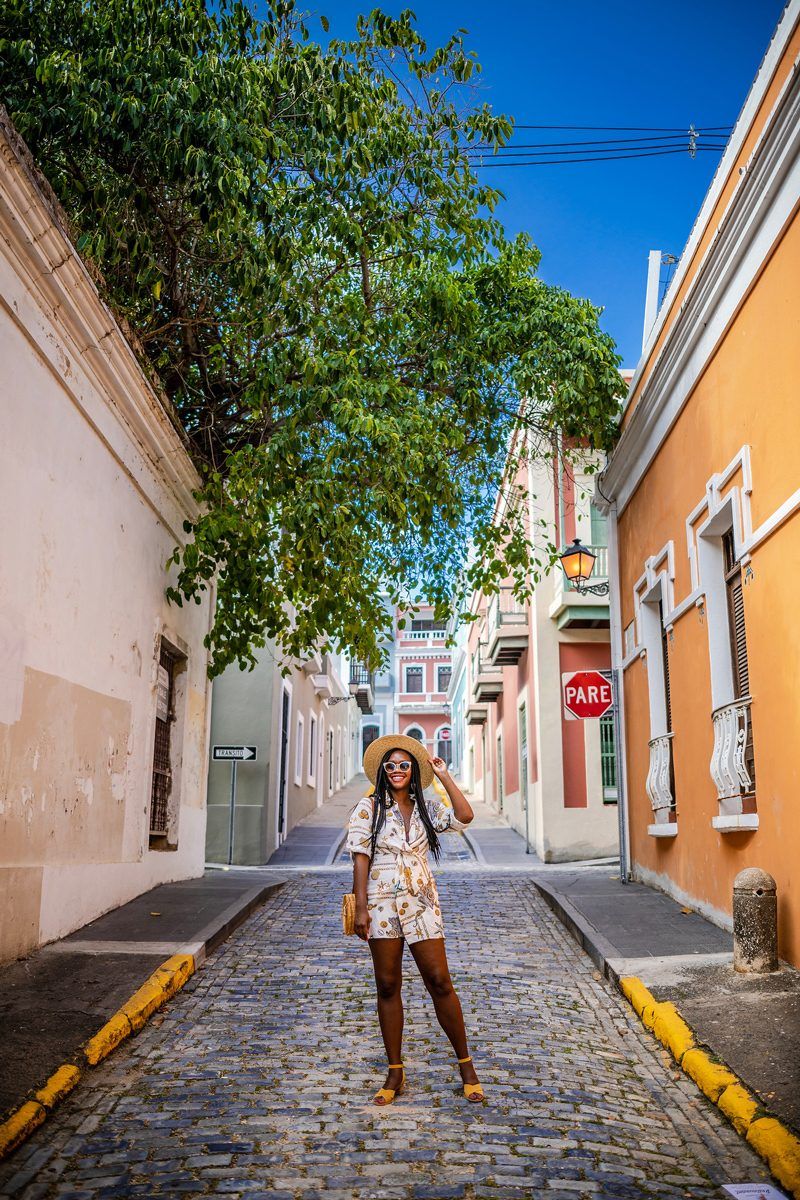 Virtual Tour Websites by popular D.C. travel blogger, Alicia Tenise: image of a woman standing on a cobble stone street next to an orange stucco building.