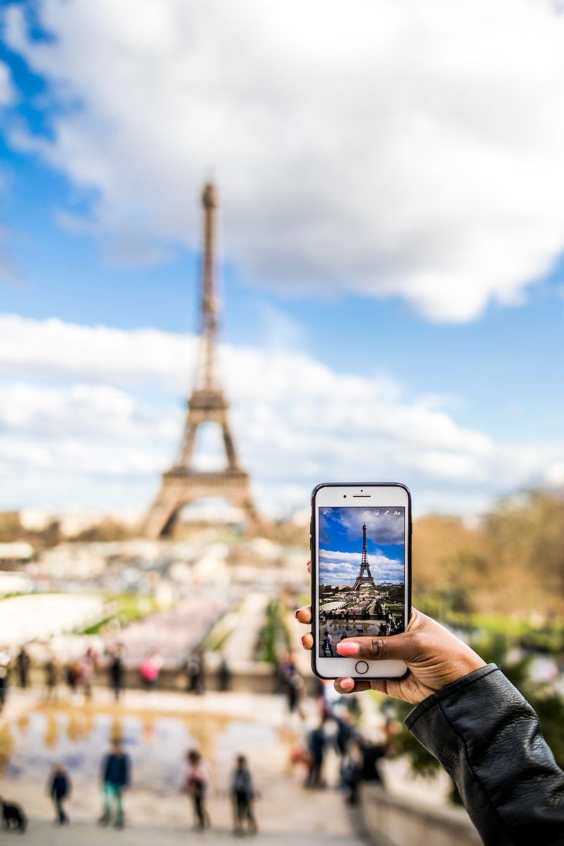 Paris Visitor's Guide | Virtual Tour Websites by popular D.C. travel blogger, Alicia Tenise: image of a woman in Paris, France taking a picture of the Eiffel Tower with her smart phone.